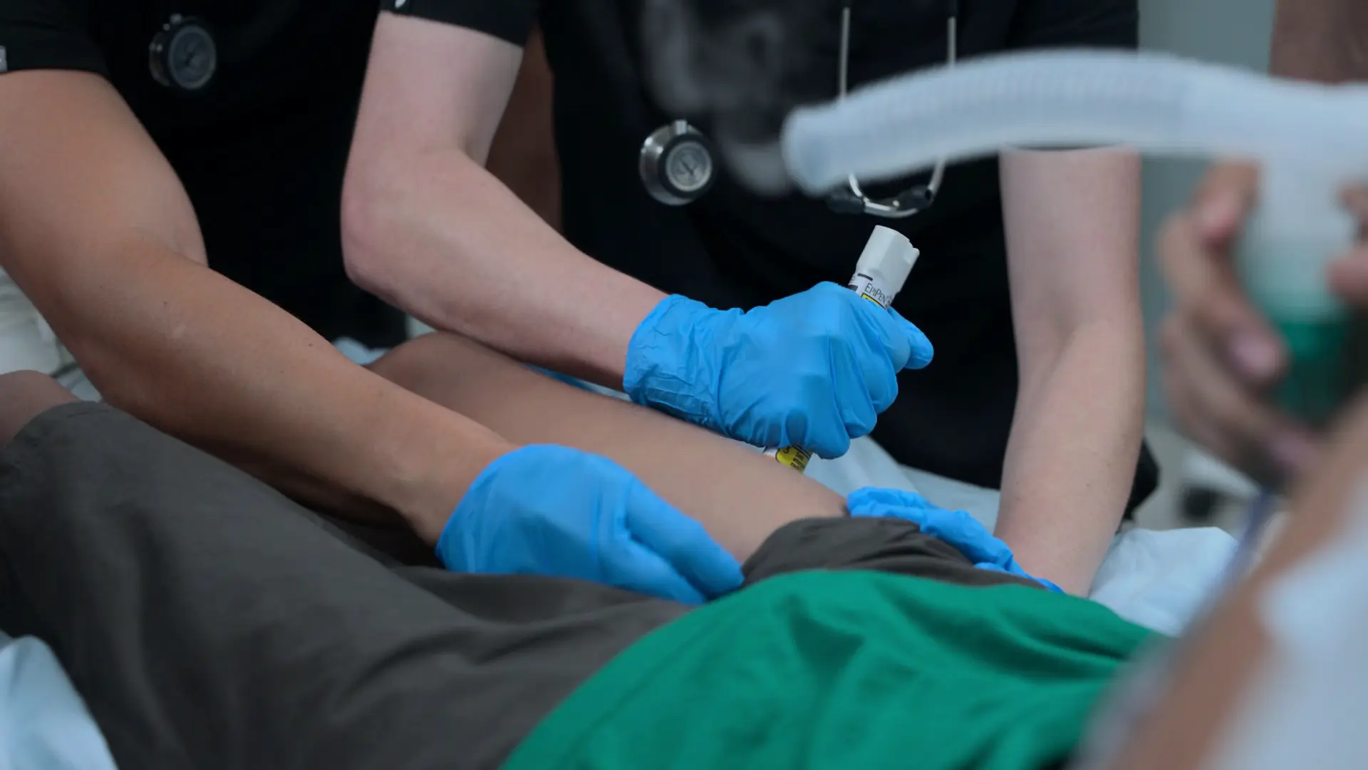Mel administrando uma caneta autoinjetora de Epinefrina intramuscular (IM) na face anterolateral da coxa do paciente.